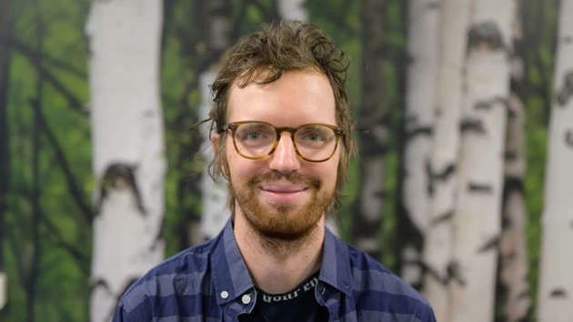 A man with a beard standing in front of a birch forest wallpaper background