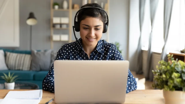 Leende kvinna med headset tittar på datorskärm.