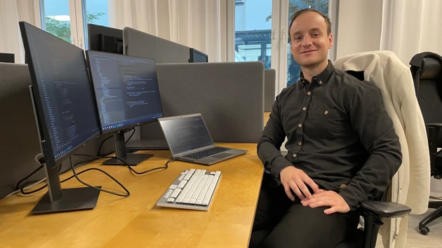 Bild på Jakub Jagiello sittande vid skrivbord omgiven av datorskärma