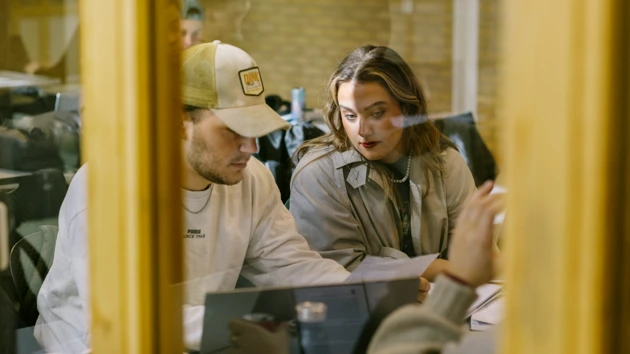 Två djupt koncentrerade studenter skriver på ett arbete tillsammans framför en laptop.