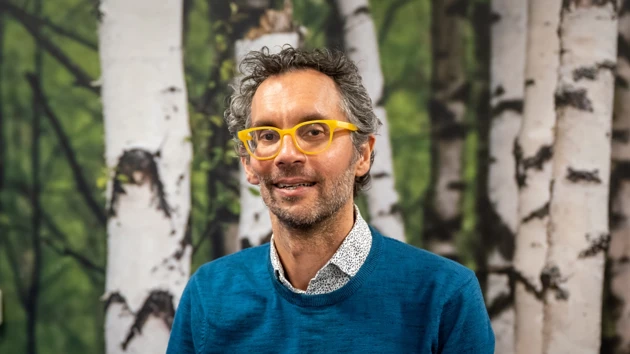 En man med glasögon står framför en målning