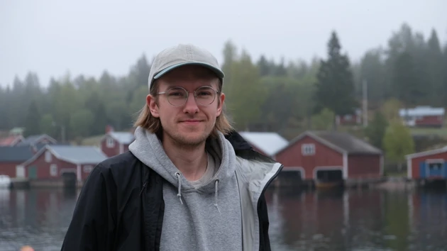 En man med hatt och glasögon står framför ett vattendrag.
