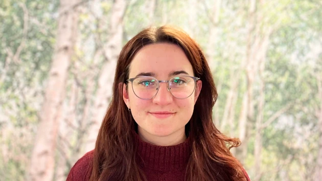 Portrait of Polona in front of a picture of birch trees.